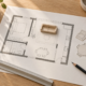Plano conceptual de una vivienda con una maqueta de sofá, recortes de muebles, una regla y un lápiz sobre una mesa.